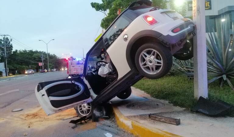Conductora de Mini Cooper de lujo, se vuela una glorieta, choca y queda atorada en un poste de concreto